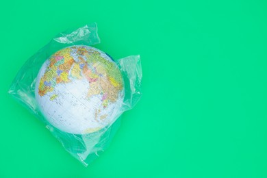 Photo of Globe in plastic bag and space for text on light green background, top view. Environmental conservation