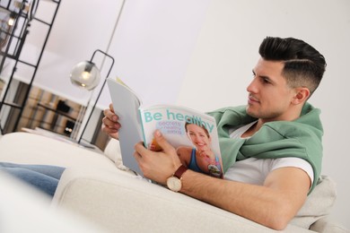 Man reading magazine on sofa in living room