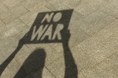 Shadow of woman holding poster with words No War outdoors