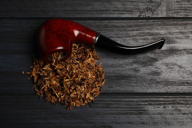 Smoking pipe and dry tobacco on black wooden table, flat lay