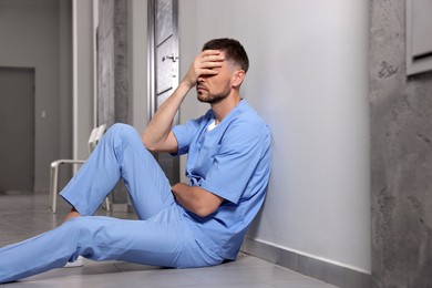 Photo of Exhausted doctor sitting near grey wall in hospital corridor