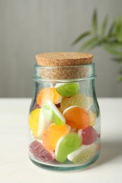 Delicious fruity gummy candies in glass jar on white wooden table