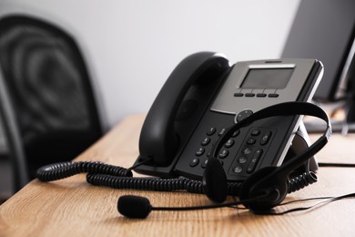 Stationary phone and headset on wooden desk in office. Hotline service