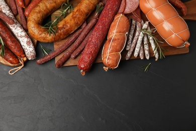 Different tasty sausages on black table, flat lay. Space for text