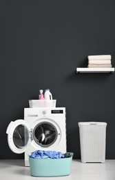 Photo of Modern washing machine, laundry basket and shelf with towels in bathroom. Space for text