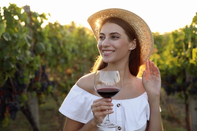 Beautiful young woman with glass of wine in vineyard on sunny day