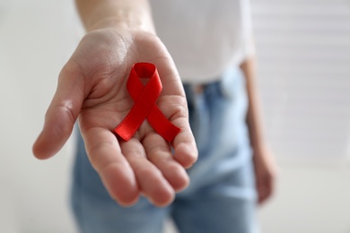 Photo of Woman holding red awareness ribbon on light background, closeup with space for text. World AIDS disease day
