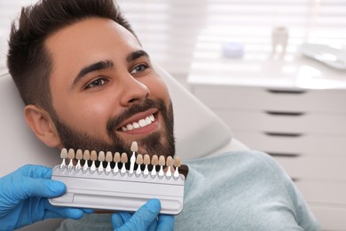 Dentist checking young man's teeth color in clinic