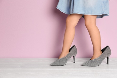 Little girl in oversized shoes near color wall with space for text, closeup on legs