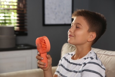 Little boy enjoying air flow from portable fan at home. Summer heat