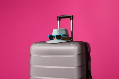 Stylish suitcase with hat and sunglasses on color background