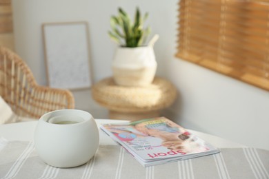 Wax air freshener with magazine on table in room, space for text. Cozy interior