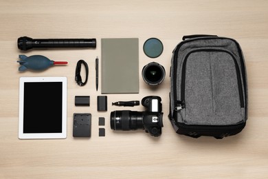 Flat lay composition with professional photography equipment and backpack on wooden table