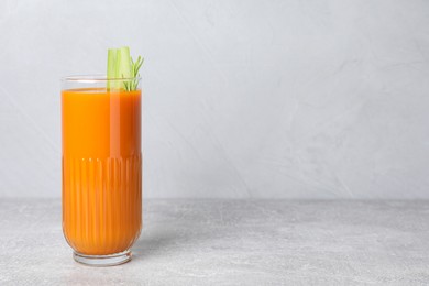 Glass of tasty carrot juice with celery sticks on light grey table, space for text