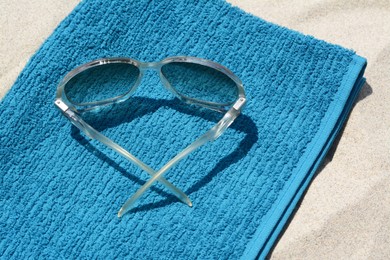 Soft blue towel and sunglasses on sandy beach, closeup