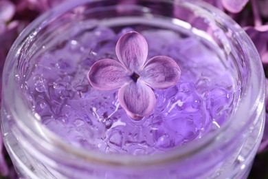 Photo of Lilac flower in jar of cosmetic product, closeup