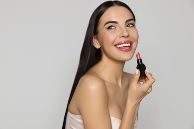 Photo of Young woman with beautiful makeup holding glossy lipstick on light gray background