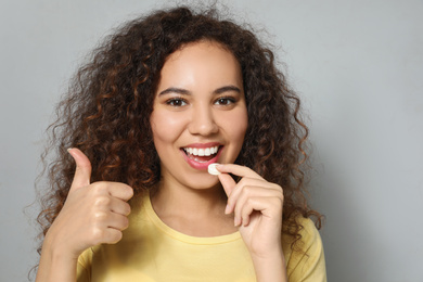 African-American woman taking vitamin pill on light grey background