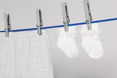 Different baby clothes drying on laundry line against light background, closeup