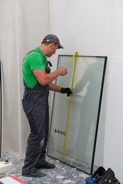 Photo of Worker in uniform measuring double glazing window indoors
