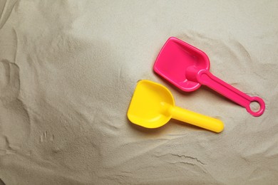 Photo of Bright plastic toy shovels on sand, flat lay
