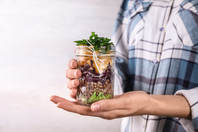 Woman holding glass jar with healthy meal, closeup