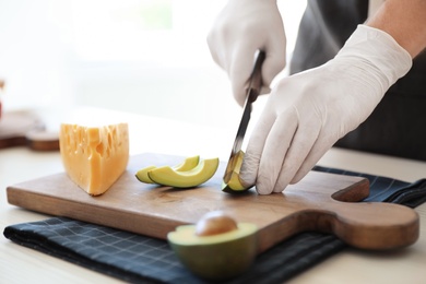 Photo of Professional chef cutting avocado on table in kitchen, closeup