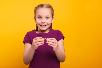 Photo of Cute girl holding tasty fortune cookie with prediction on orange background