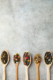 Different kinds of dry herbal tea in wooden spoons on light grey table, flat lay. Space for text