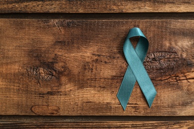 Teal awareness ribbon on wooden background, top view with space for text. Symbol of social and medical issues