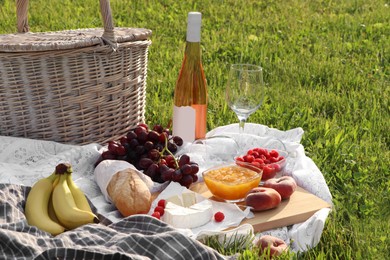 Picnic blanket with tasty food, basket and cider on green grass outdoors