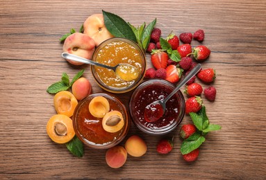 Jars with different jams and fresh fruits on wooden table, flat lay