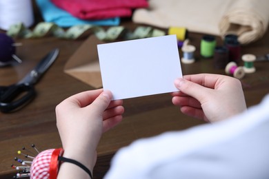 Photo of Seamstress holding blank card over table in atelier, closeup. Space for text