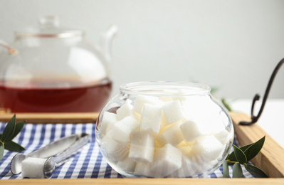 Refined sugar cubes in glass bowl and tongs on wooden tray