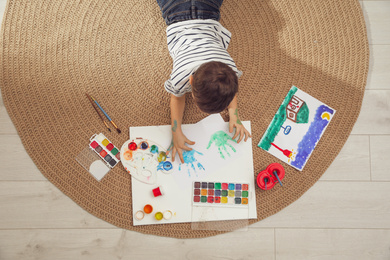 Little child painting on floor at home, top view
