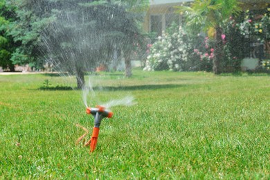 Photo of Automatic sprinkler watering green grass in park. Irrigation system