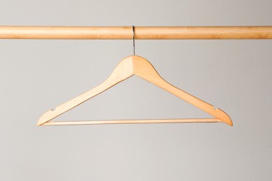 Empty clothes hanger on wooden rail against light grey background