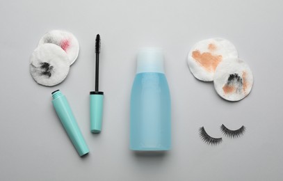 Dirty cotton pads, eyelashes, mascara and makeup removal product on light grey background, flat lay