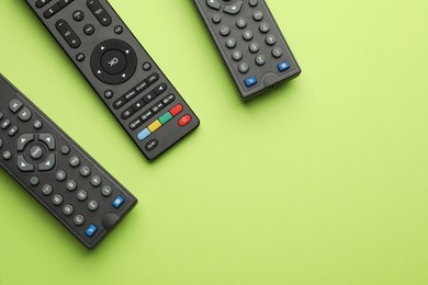 Remote controls on light green background, flat lay. Space for text