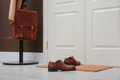 Stylish shoes on door mat near coat rack in hall