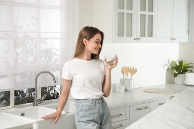 Woman drinking tap water from glass in kitchen