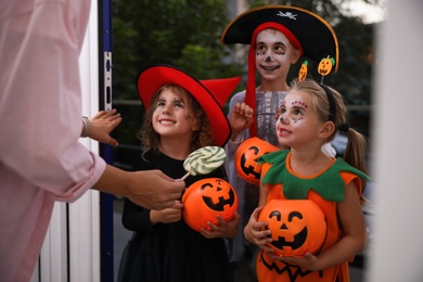 Cute little kids wearing Halloween costumes and trick-or-treating at doorway