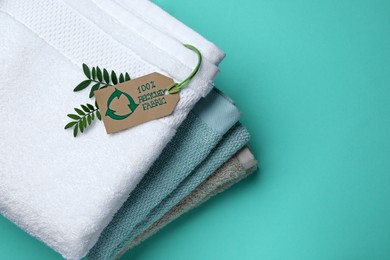 Stacked towels with recycling label and plant on turquoise background, top view. Space for text