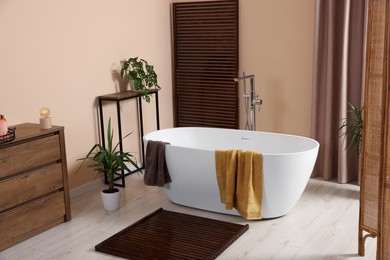 Stylish bathroom interior with ceramic tub, terry towels and houseplants