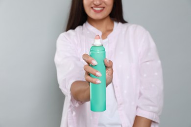 Woman with dry shampoo bottle on light grey background, closeup