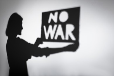 Shadow of woman holding poster with words No War on light background