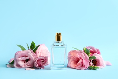 Bottle of perfume and beautiful flowers on light blue background
