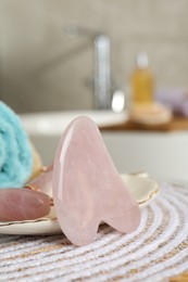 Photo of Rose quartz gua sha tool and natural face roller on table in bathroom, closeup