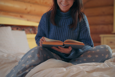 Young woman in warm sweater reading book on bed at home, closeup