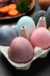 Photo of Easter eggs painted with natural organic dyes on black table, closeup